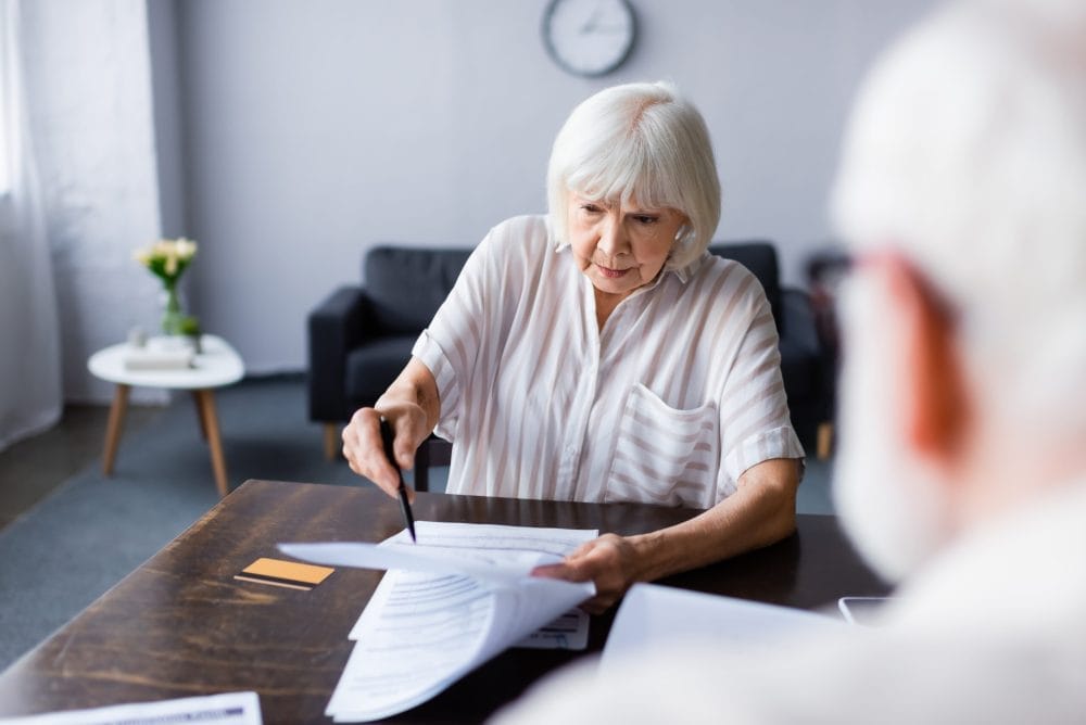 Do seniors over 70 need to do federal tax returns every year? - Selective focus of senior woman holding pen and papers near credit card and husband at home