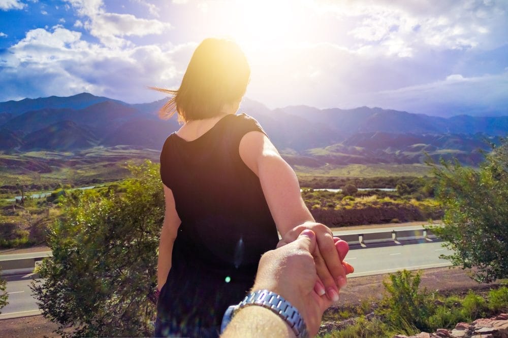 A woman holding her boyfriend's hand and walking in front of him
