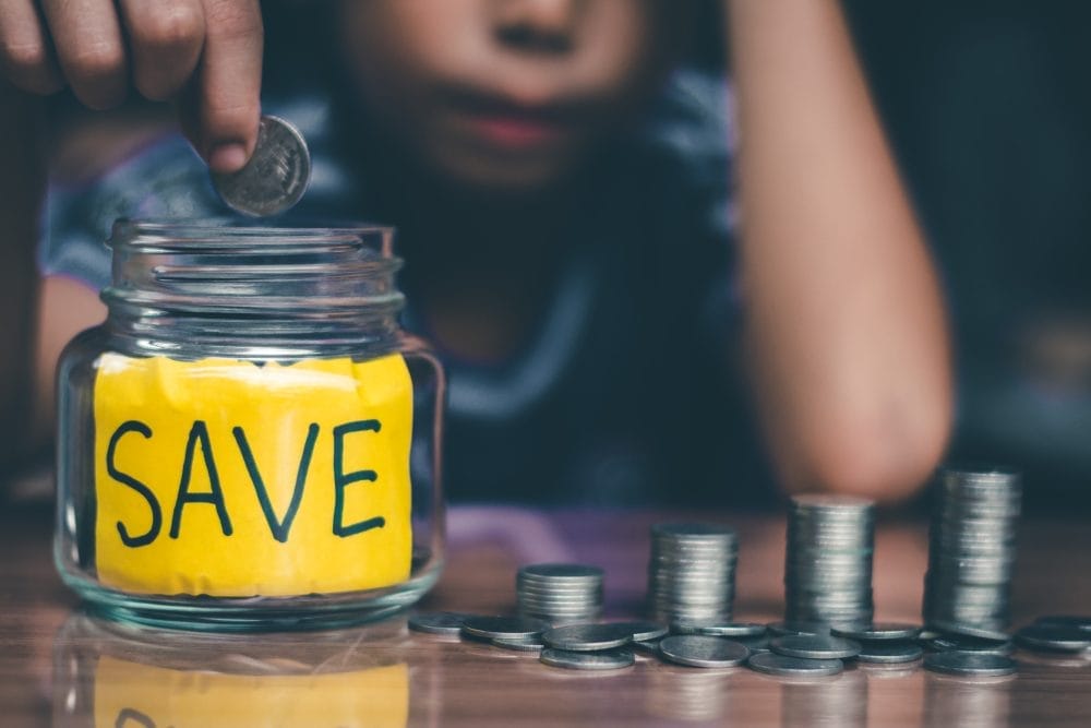 A woman putting money into a jar that says, "Save"