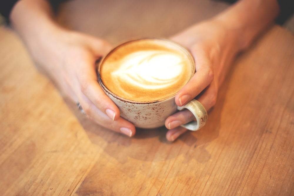 Two hands wrapped around a mug of gourmet coffee
