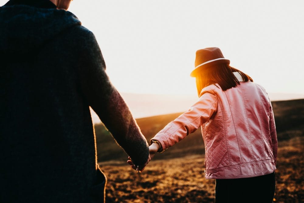 woman with a hat holding her boyfriend's hand