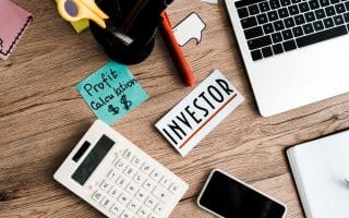A desk filled with a calculator, laptop, and a piece of paper that says "Investor"