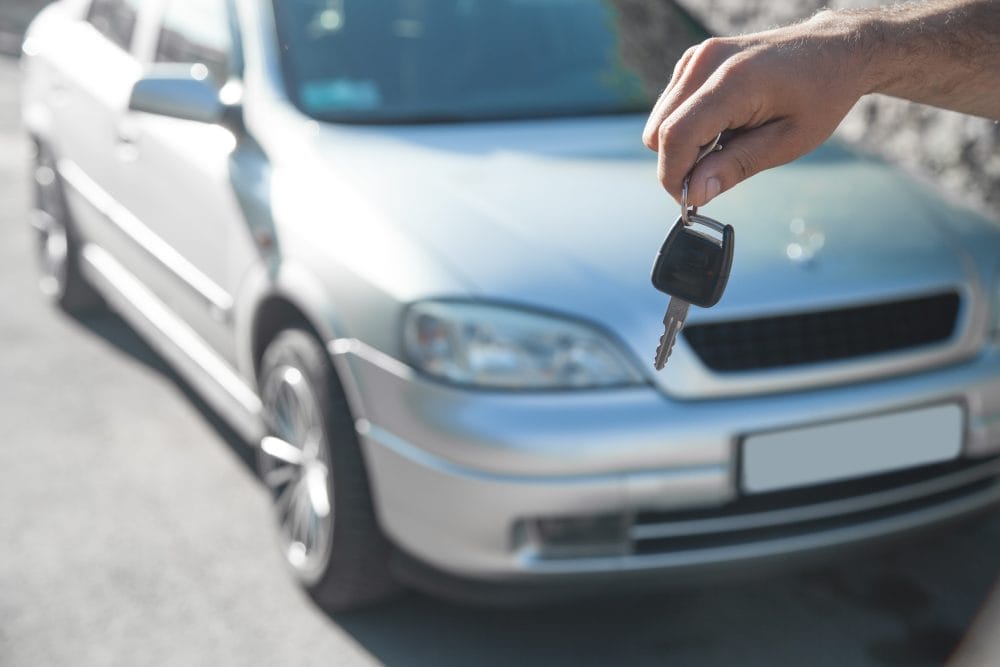Someone holding keys in front of a used car