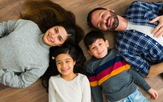 Mother and father and two small children smiling and laying on the floor