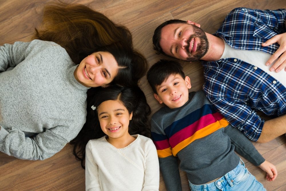 Mother and father and two small children smiling and laying on the floor