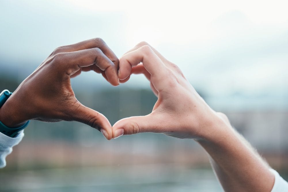 Outdoor, closeup and people with heart sign, hands and support with kindness, emoji and commitment. Outside, couple or interracial with symbol for love