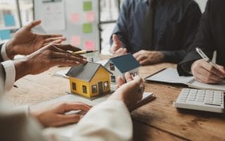 Two model homes on a table with people discussing them