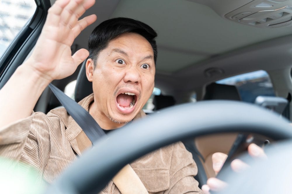 A man is yelling in a car is driving a car and looking at his cell phone. He is surprised and excited. Concept of distraction while driving and the potential danger it poses.