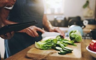 Hands, tablet and salad recipe in kitchen with help, support and teaching at home for healthy food. People cooking lunch on digital tech for nutrition tips with lettuce, cucumber and green vegetables.