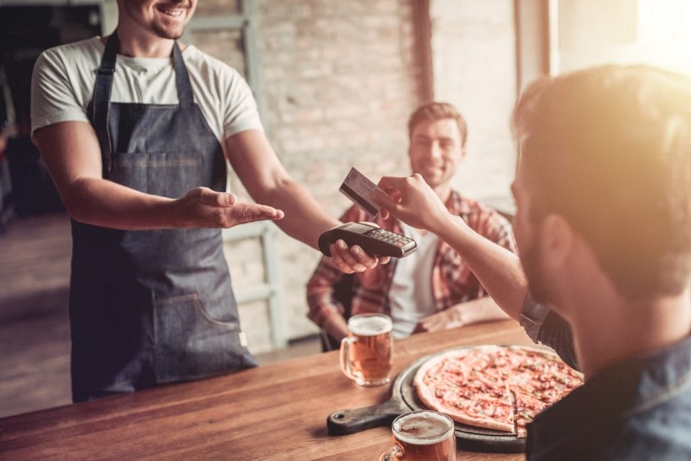 Man paying for pizza at a restaurant with a friend