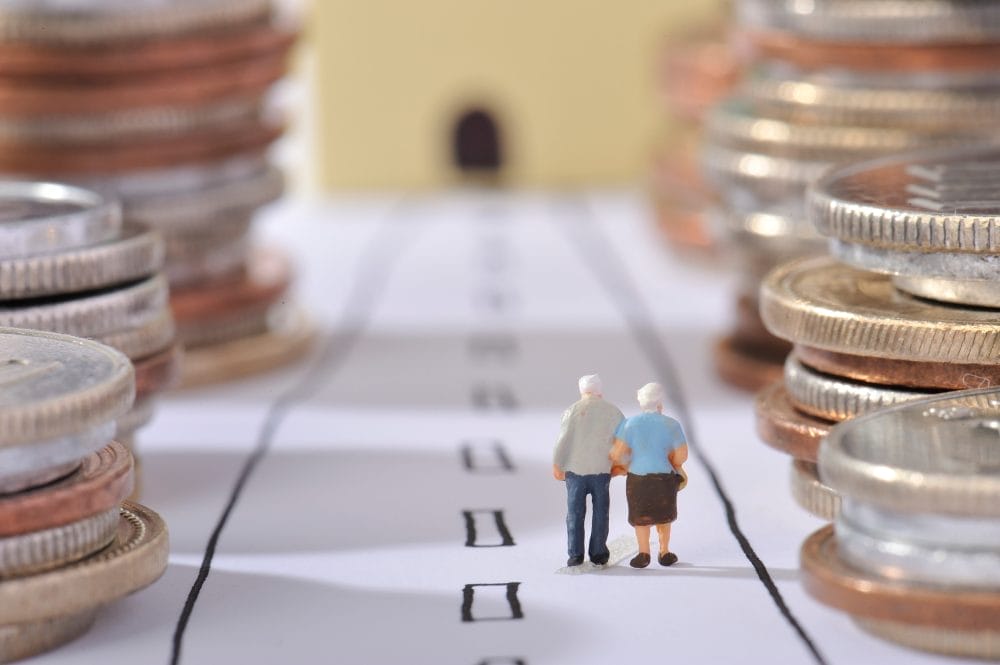 A pair of small dolls of elderly people next to stacks of coins