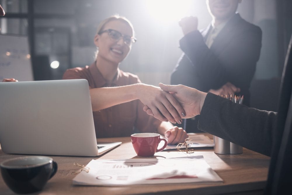 A woman shaking hands with a work associate at a meeting