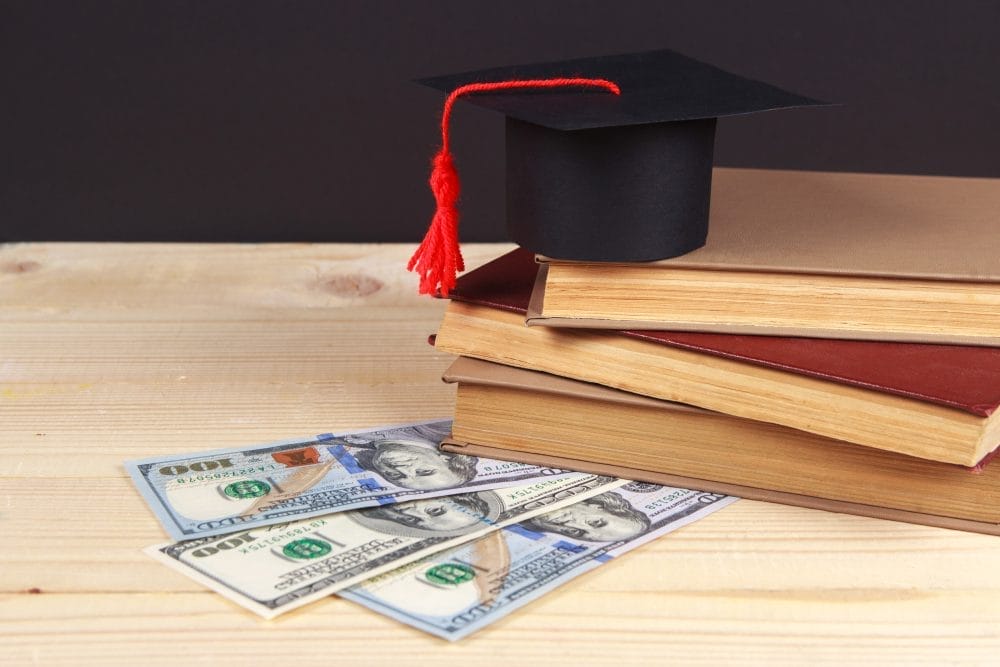 Money with books and a graduation cap on top of it