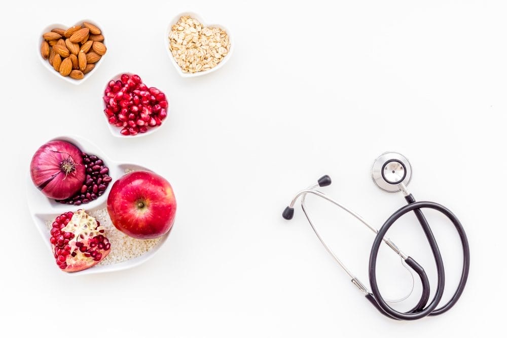 Products good for heart and blood vessels. Vegetables, fruits, nuts in heart shaped bowl near stethoscope on white background top view.