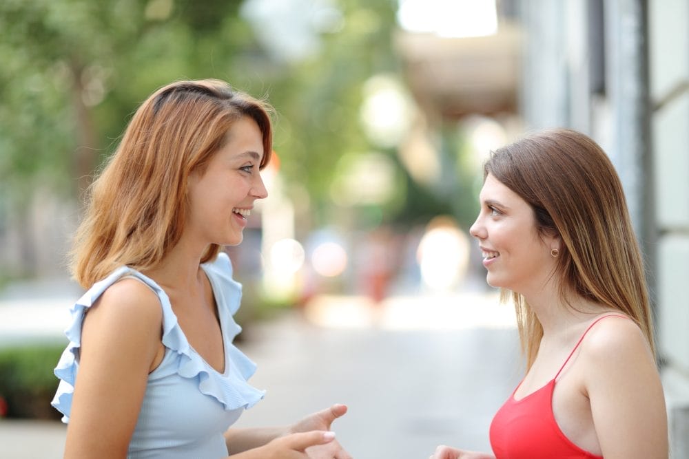 Profile of two happy friends talking and smiling in the street