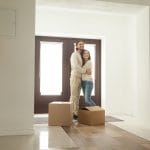 Happy young millennial couple hugging standing near boxes moving into new home, smiling homeowners embracing in modern hallway just moved in own house, mortgage investment and relocation concept