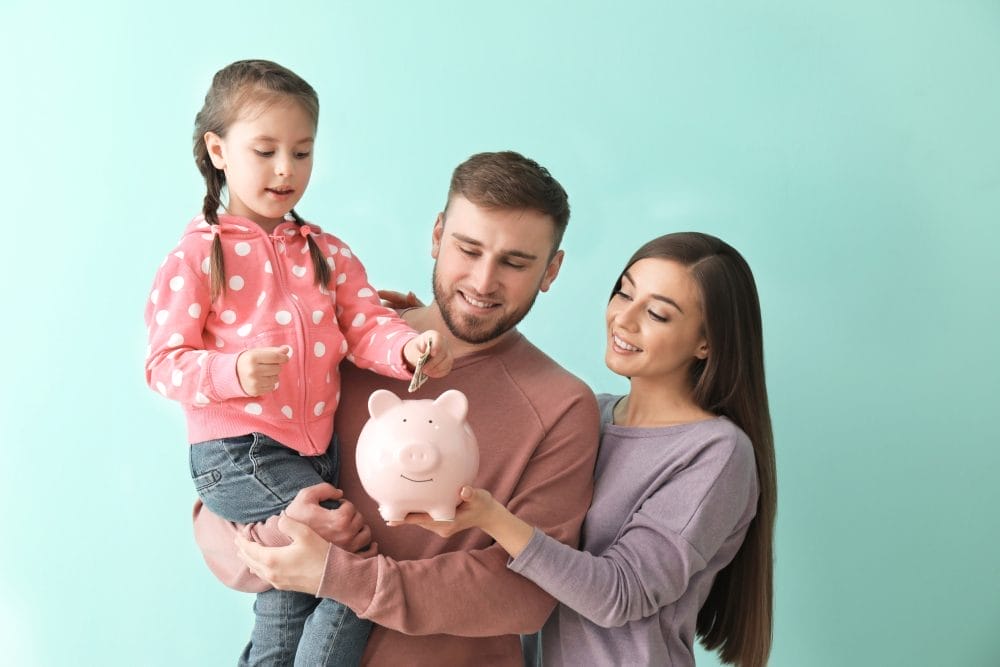 A young couple holding up their child with a piggy bank