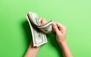 Businesswoman's hands counting one hundred dollar bills on colorful background.