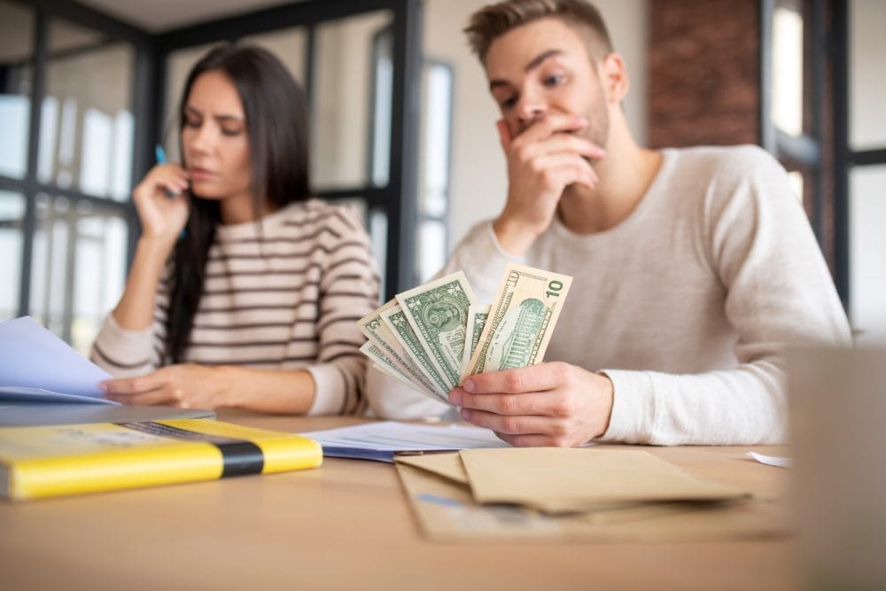 A young man holding cash and contemplating