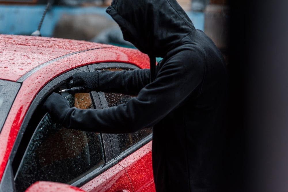 A car thief attempts to break into the window of a red car