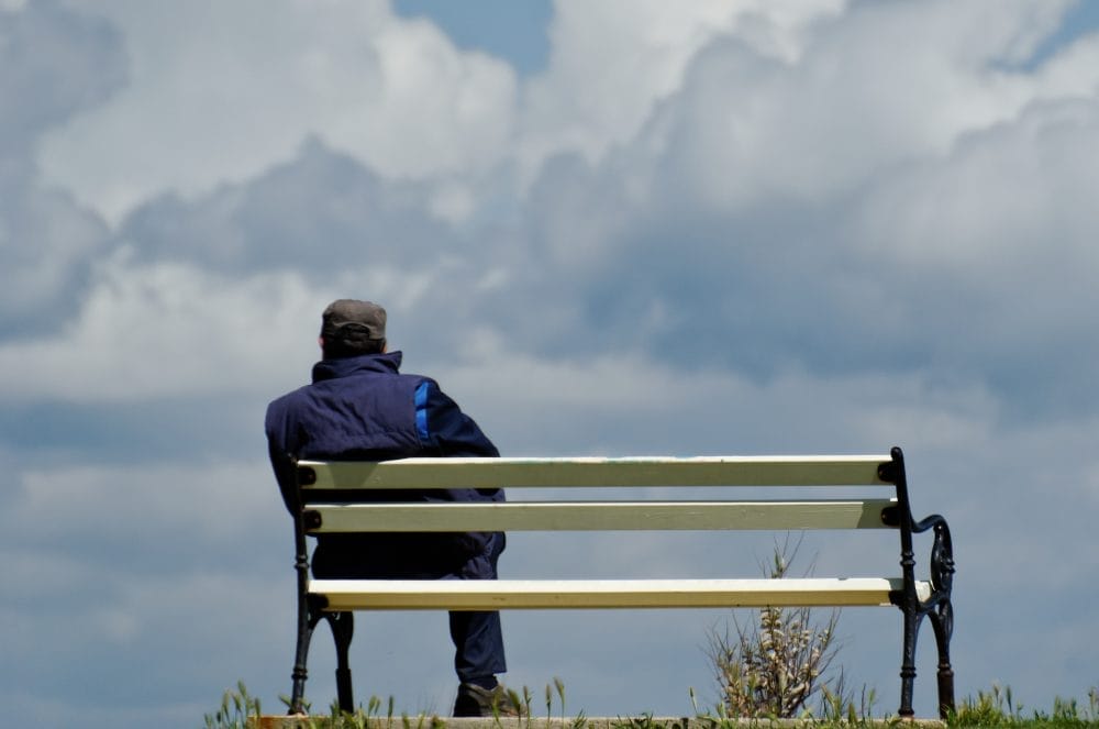 An older man sitting alone on a bench outside
