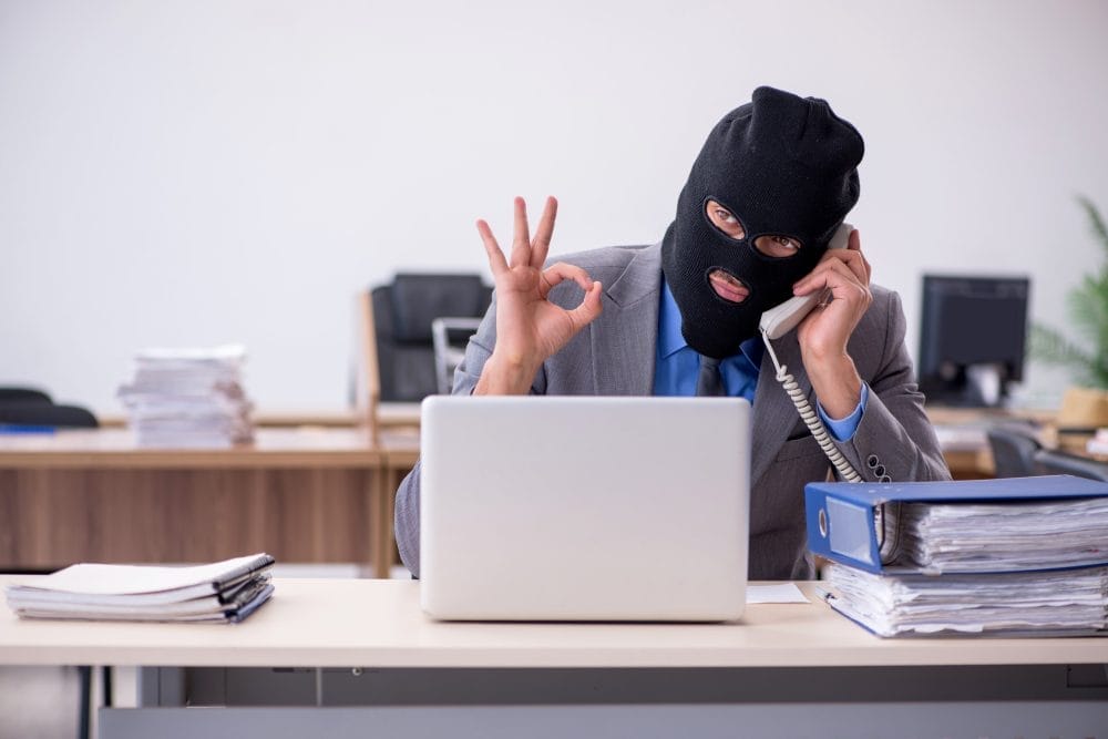 A young male man in a mask attempting to make a computer scam to hurt an older woman
