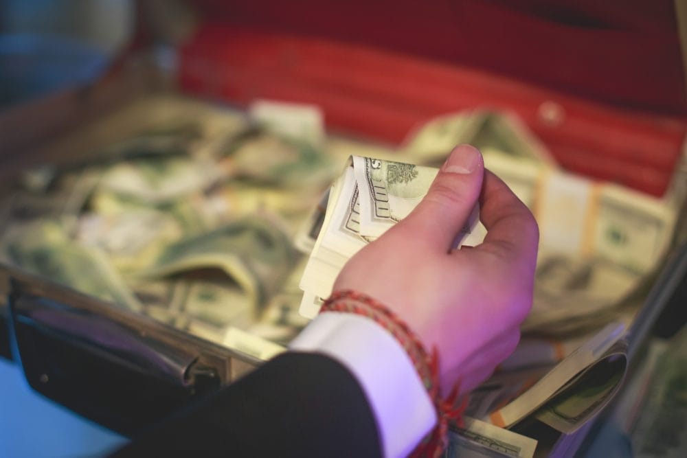 A man holding a pile of cash, trying not to self-sabotage himself and lose it