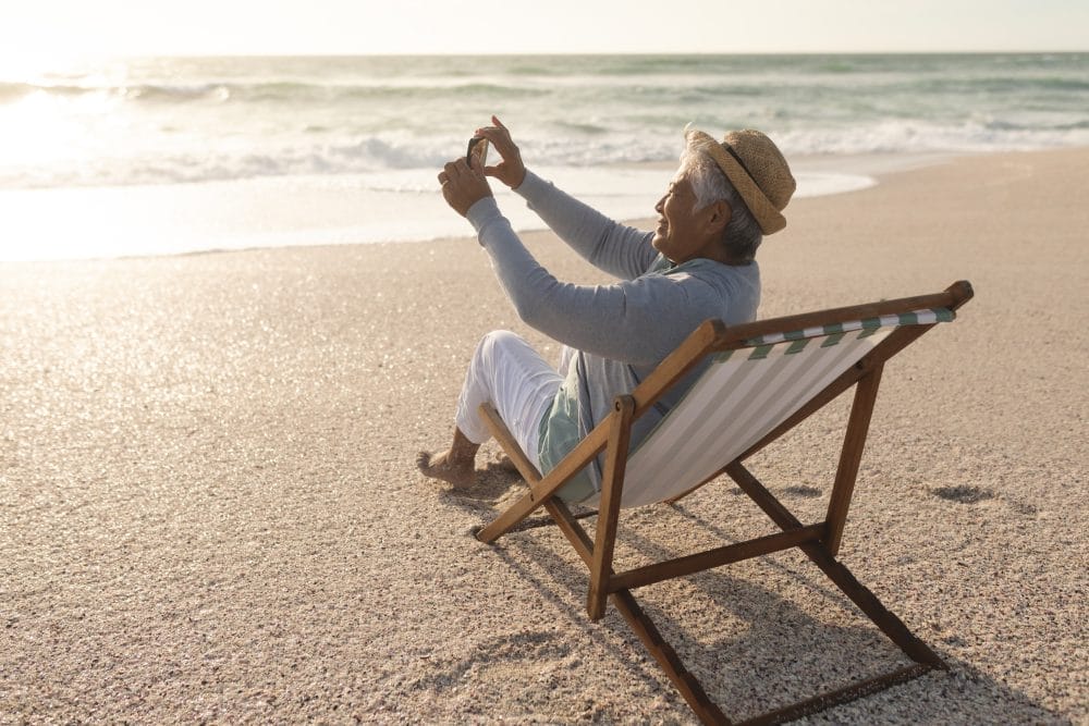 Senior retired woman sitting on the beach taking a photo