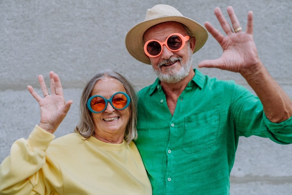 A couple of happy seniors in colourful clothes waving at camera.