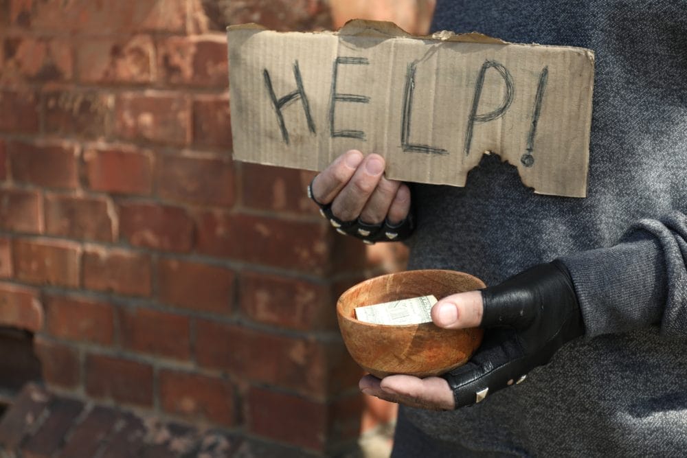 Poor homeless man holding help sign and bowl with donations outdoors. 