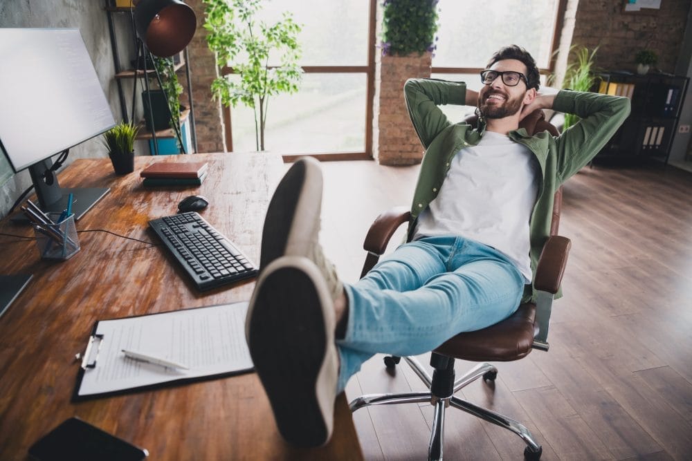 A remote worker at home, smiling and kicking up his feet on his desk