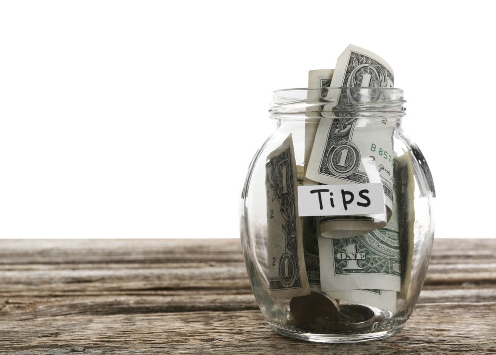 Glass jar with tips on wooden table against white background