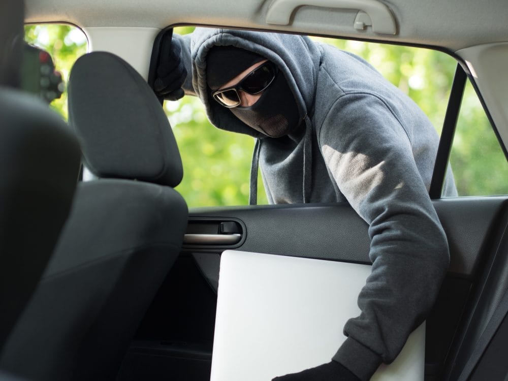 A criminal breaking into a car after putting a flyer on the windshield