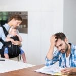 Frustrated dad looking at bills while his wife takes his child outside