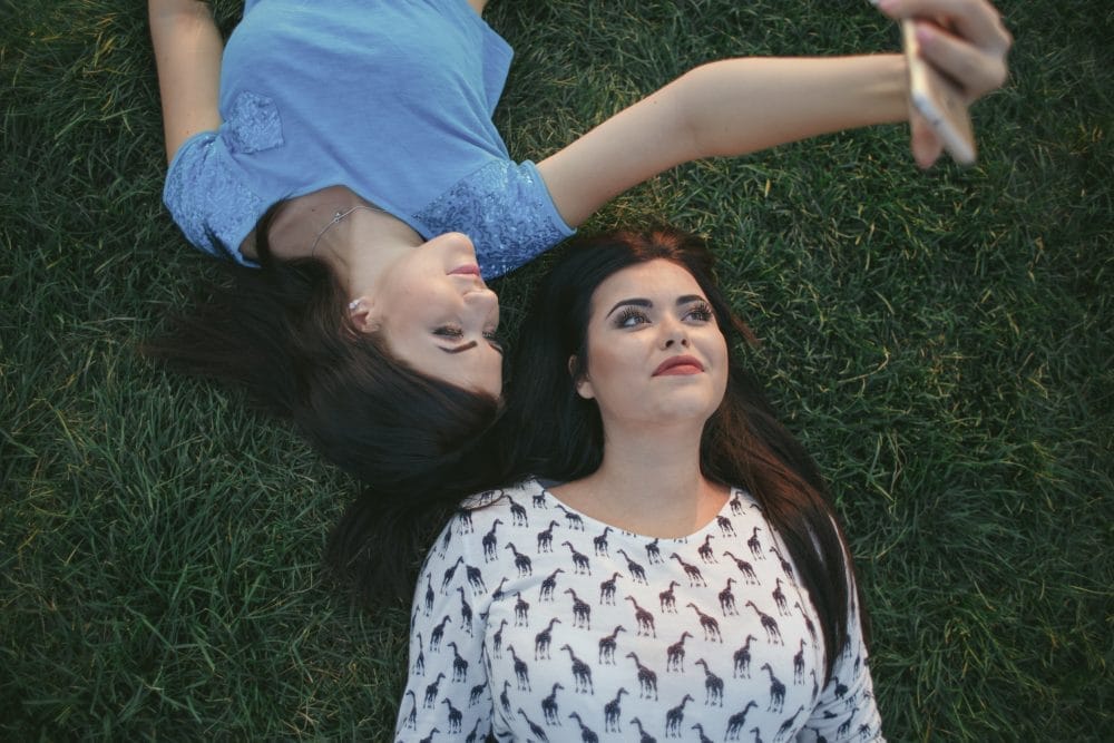 Two girls laying in the grass taking selfies