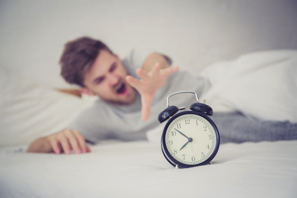A man struggling to reach his alarm clock