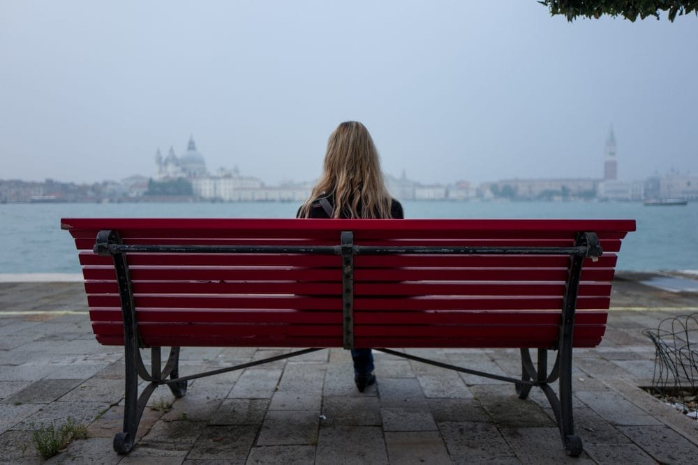 Blonde girl on park bench looking at water