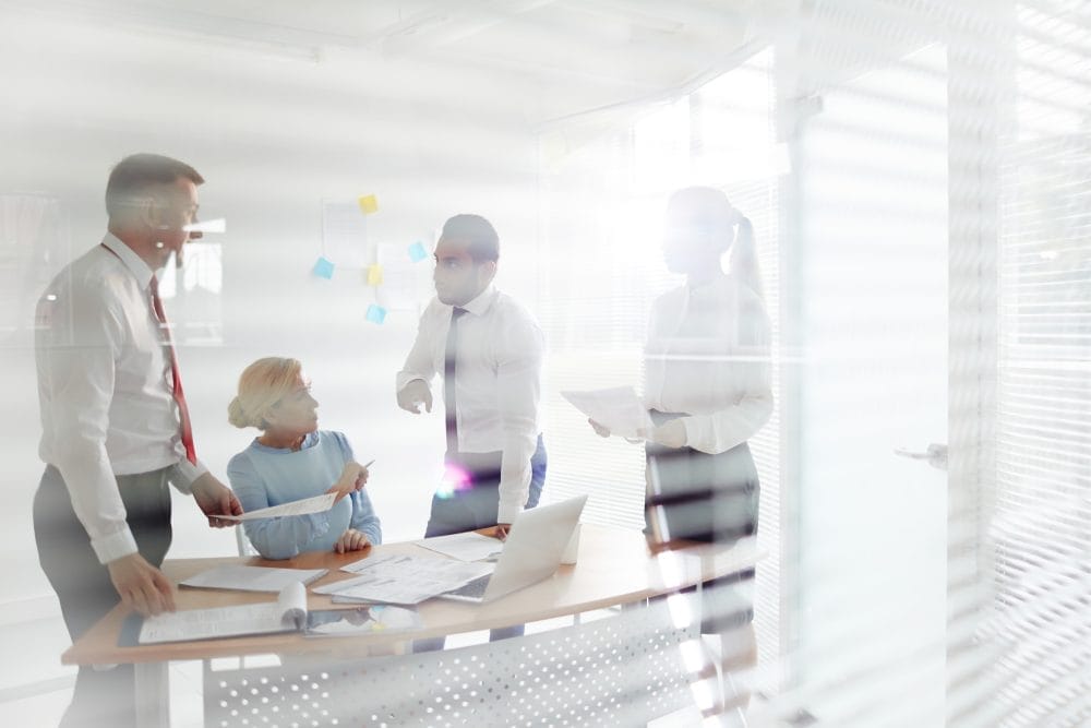 Four colleagues with papers discussing work at a meeting