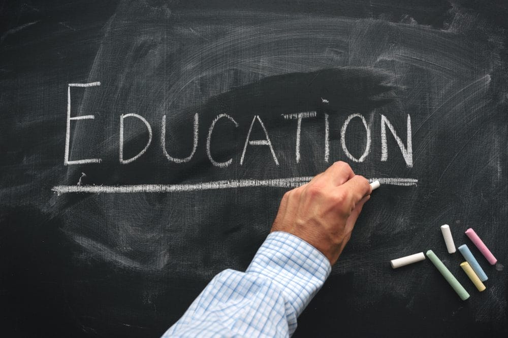 A teacher writing "education" on a chalkboard. Education is an industry that is using AI more often in disturbing new ways.