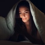 A woman using her phone in bed, which is an everday decision that is costing you years off your life