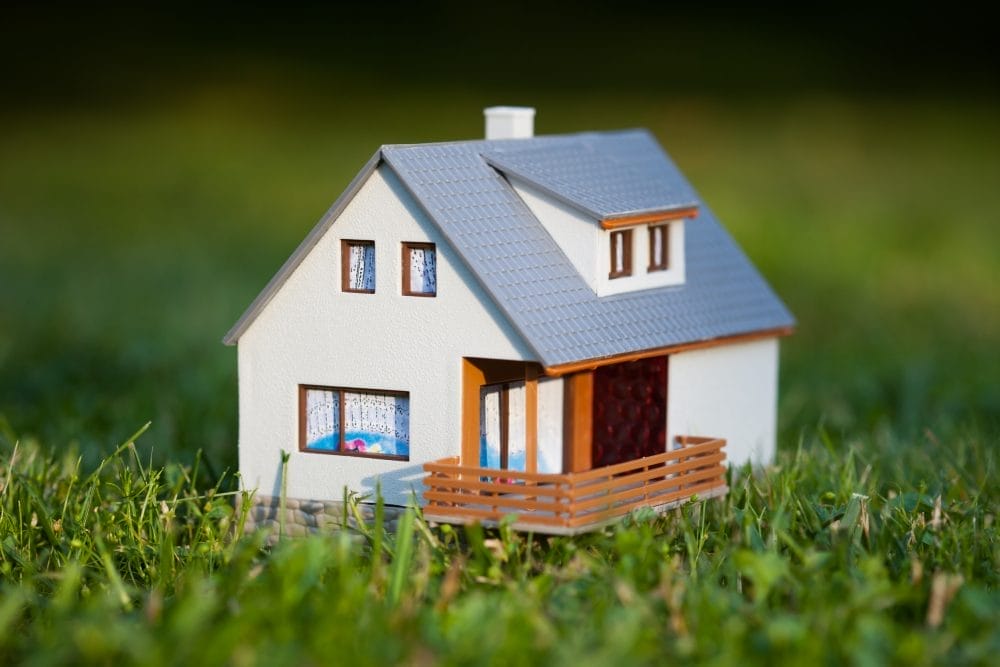 A small model home in the green grass, possibly covered by a warranty