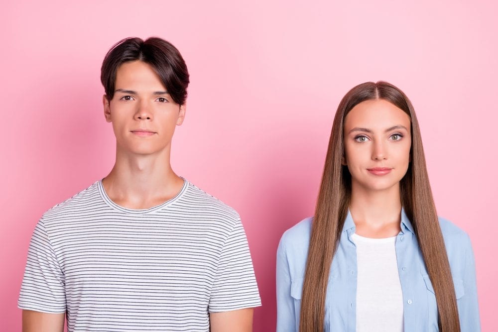 Two siblings in front of a pink background who are jealous of each other, and not because of money