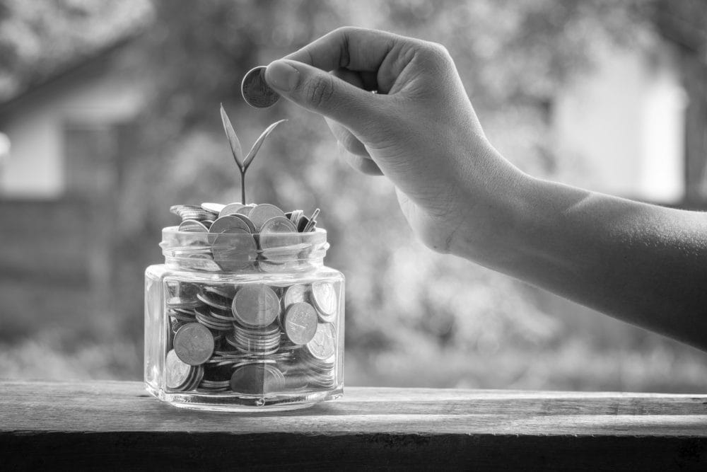 A young person dropping a coin into a jar to secure financial future